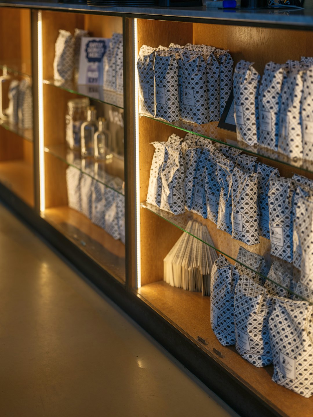 Display cabinet with coffee bags and bottles on illuminated shelves.